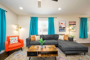 A living room with a grey sectional sofa, a red armchair, a wooden coffee table, and teal curtains.
