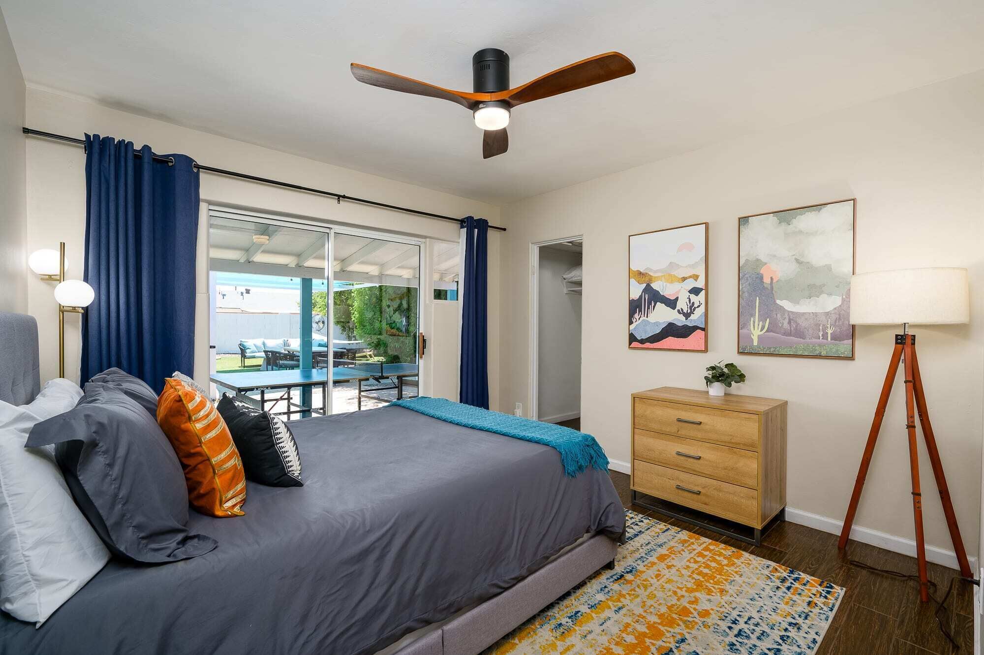 Ein modernes Schlafzimmer mit Bett, Deckenventilator, Schreibtisch und Blick ins Freie.