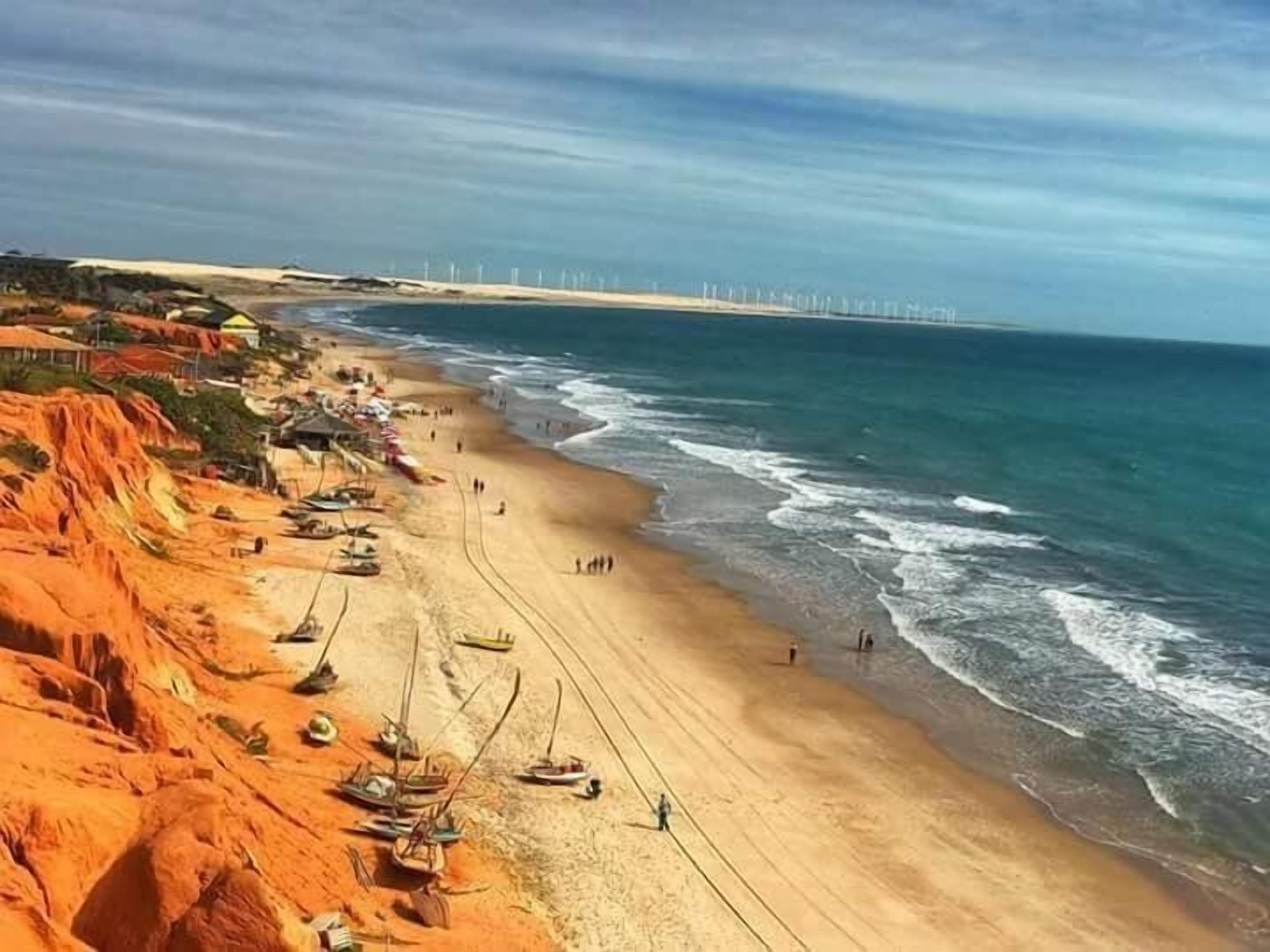 Uma praia com barcos e um parque eólico ao longe.