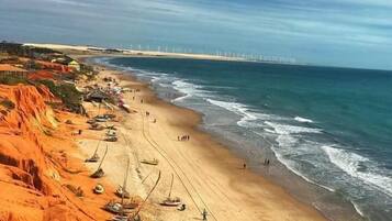 Uma praia com barcos e um parque eólico ao longe.