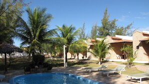 A swimming pool with lounge chairs, palm trees, and a brick building with a tiled roof. - POUSADA 7 MARES (Aracati)