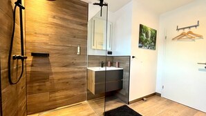 A modern bathroom with a wooden shower enclosure, a glass partition, a sink with a mirror, and a black rug. - App. 5 - wohlB2 (3 Zi, 2 adult + 2 kids) (Braunlage)