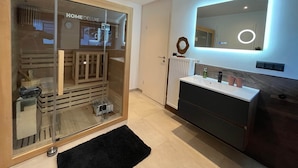 Un baño moderno con cabina de ducha de vidrio, un espejo grande con iluminación LED y un mueble de tocador oscuro.