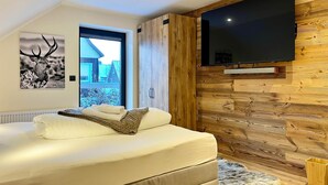Un dormitorio con cama, pared de madera, televisor y ventana con vista a una casa.