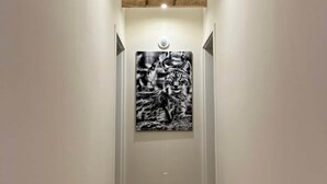 Un estrecho pasillo con vigas de madera en el techo, una fotografía blanco y negro enmarcada en la pared, y una lámpara colgante.
