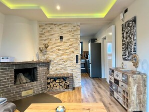 Una sala de estar moderna con pared de piedra, chimenea, piso de madera y mueble empotrado para entretenimiento.