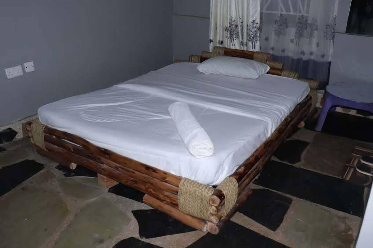 Ein Bett mit weißer Matratze, einem zusammengerollten Handtuch, einem Holzrahmen und einem bodenähnlichen Steinmuster.