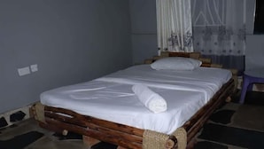 Una cama con estructura de madera y ropa de cama blanca, una cortina y un papel tapiz estampado.