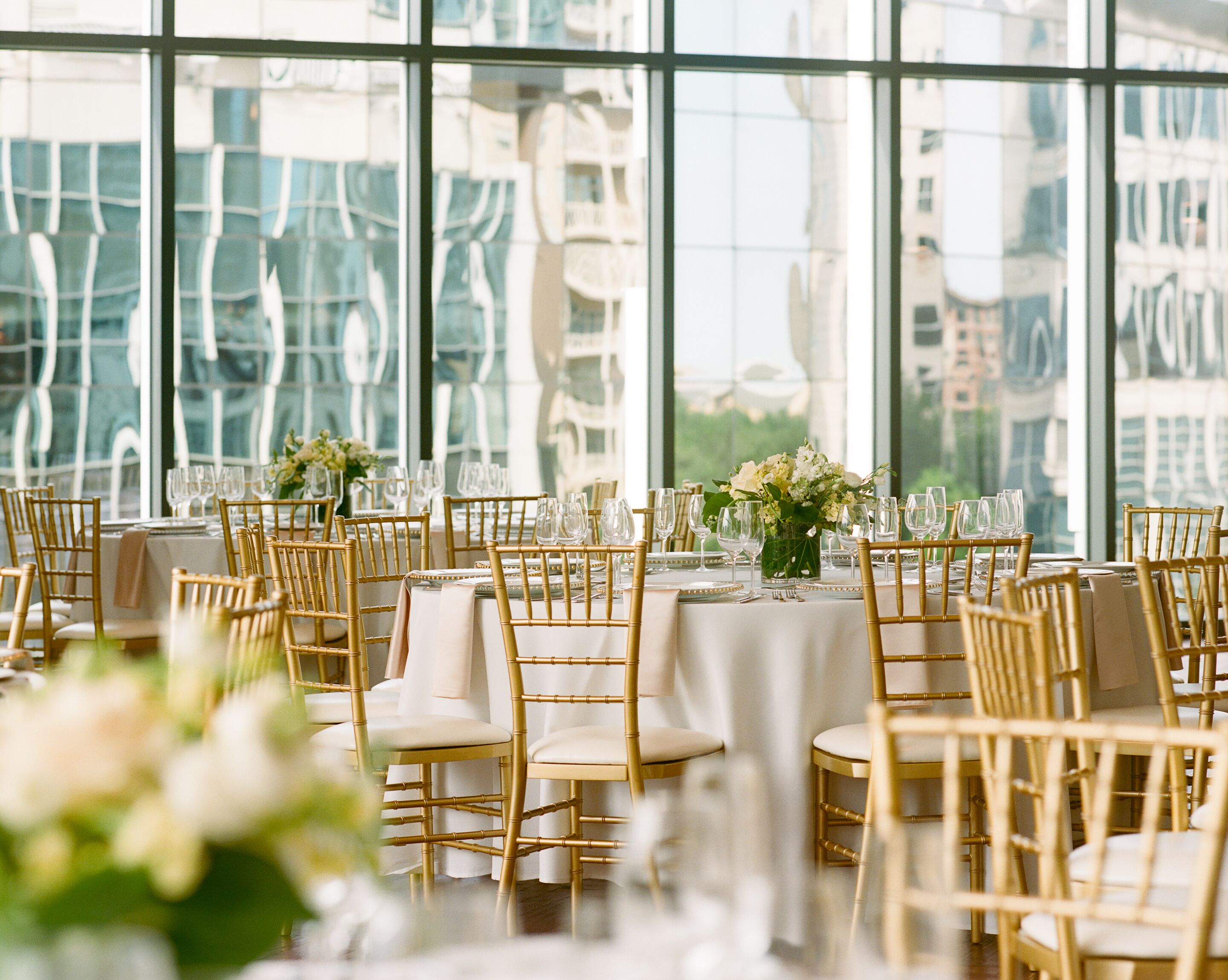 Een feestzaal met gedekte tafels voor een formeel evenement, grote ramen met uitzicht op de stad.