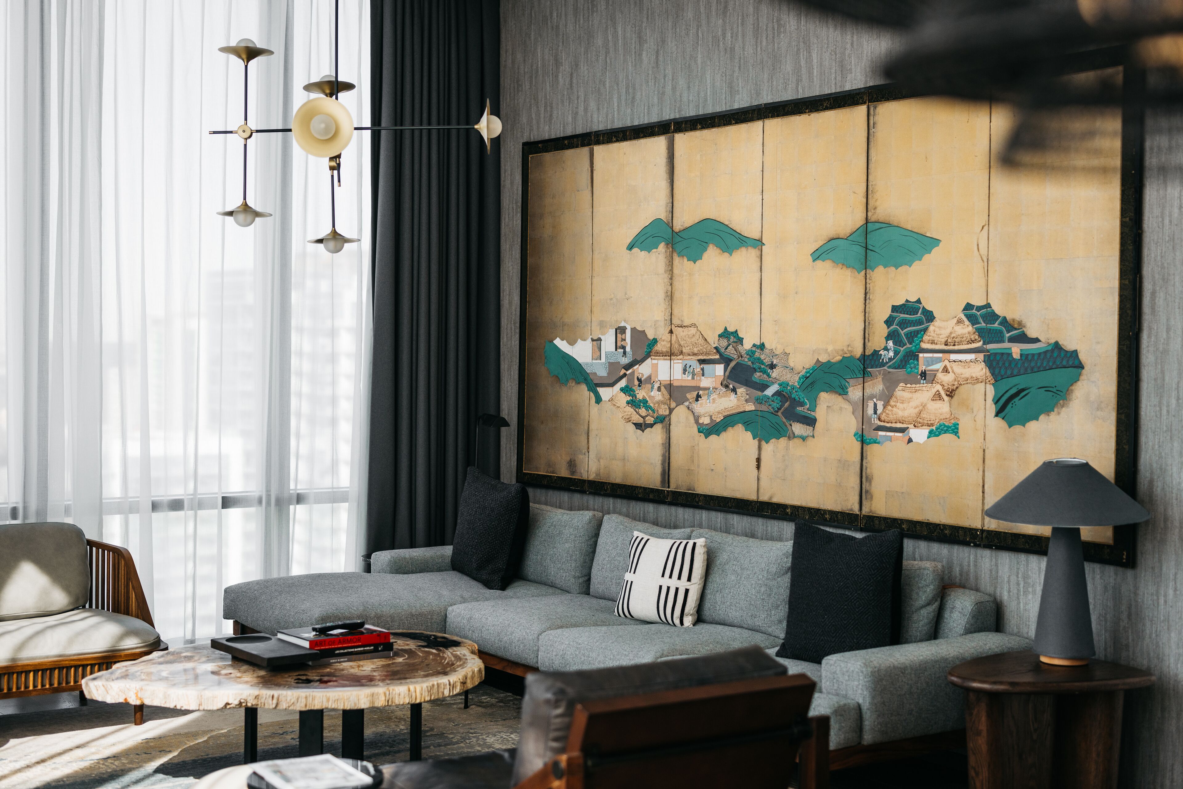 Een moderne woonkamer met een grijze bank, een ronde salontafel en een groot abstract schilderij aan de muur.
