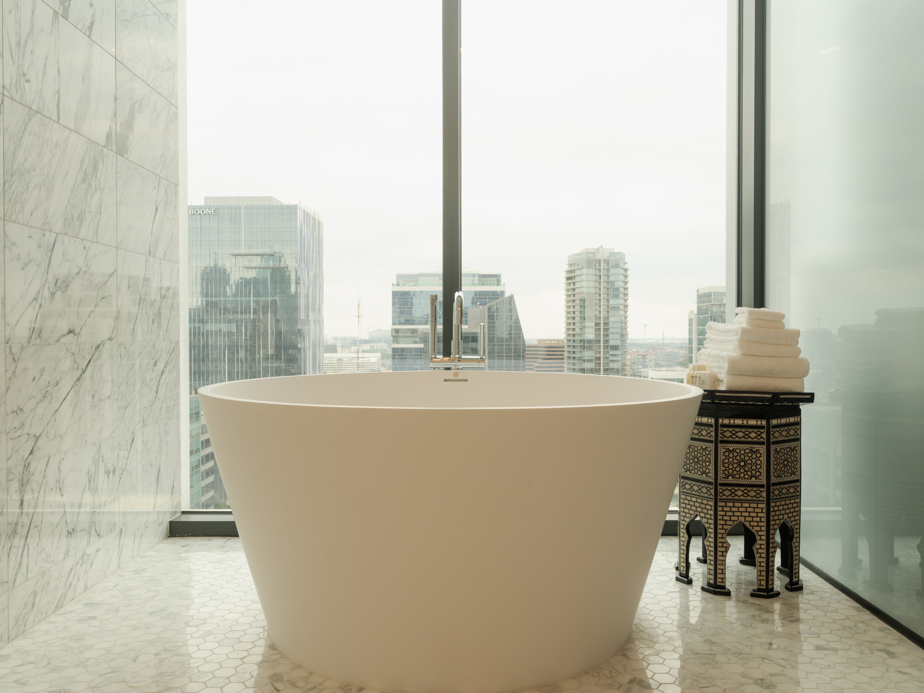 Une salle de bain moderne avec une baignoire îlot, une fenêtre encadrée de verre et un banc décoratif recouvert de carreaux.