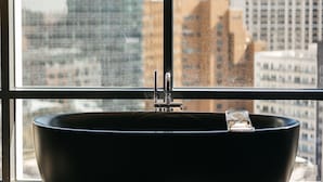 A modern bathroom with a large black bathtub, a window with a view of a cityscape, and a visible faucet. - Hôtel Swexan (Dallas)