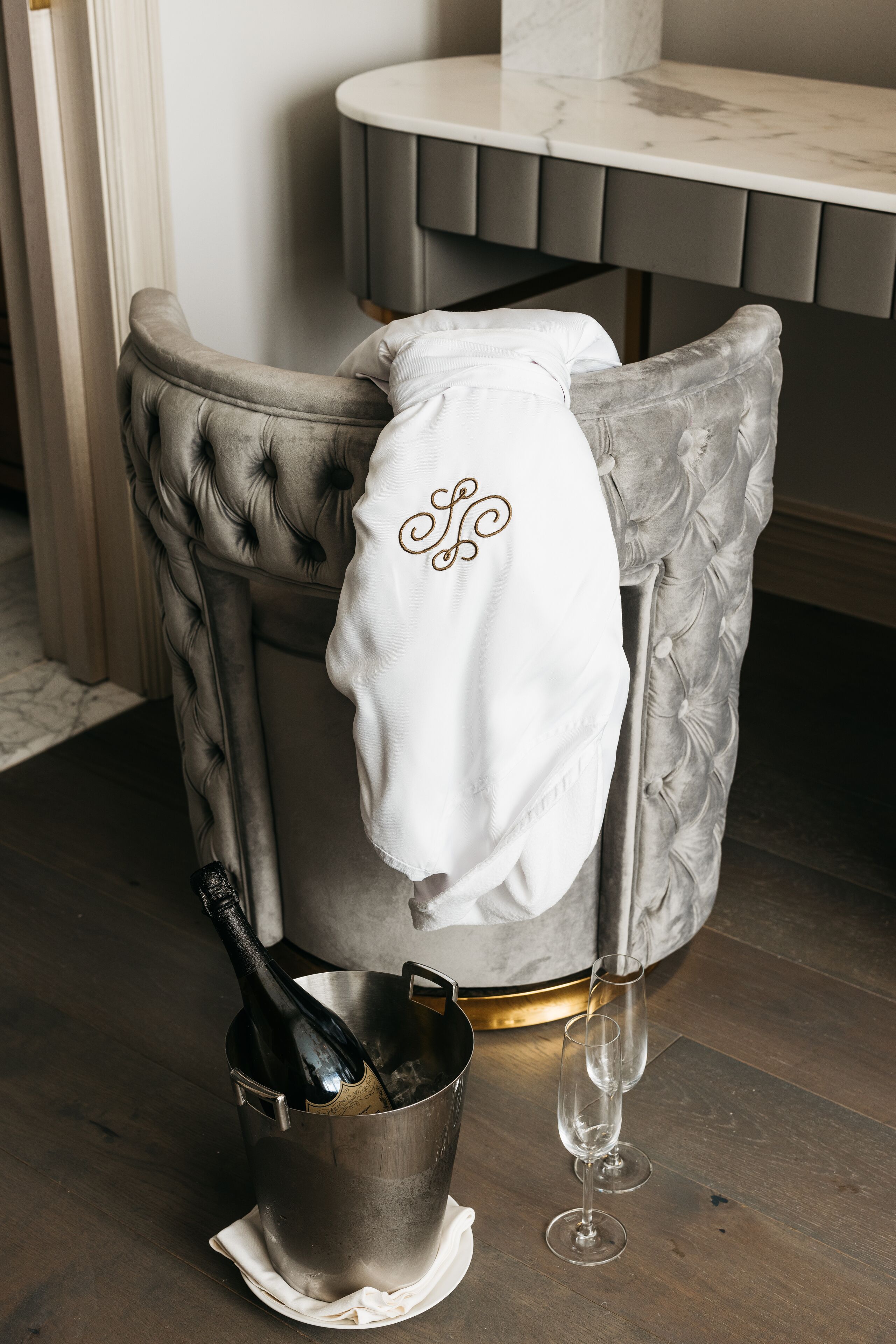 A chair with a white towel draped over it, a bottle of champagne, and two champagne glasses in a metal bucket.