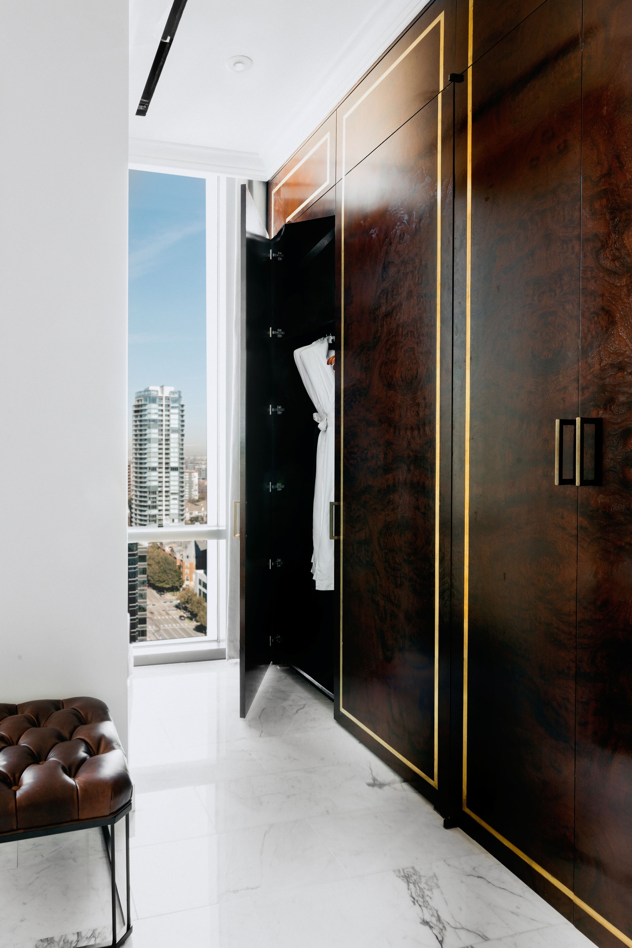 Ein modernes Interieur mit großem Kleiderschrank, einer Lederausstattung und Blick auf eine Skyline durch ein großes Fenster.