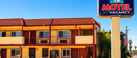 A two-story motel with a red and yellow facade, a signboard indicating no vacancy, and a parking lot with a handicapped parking space.