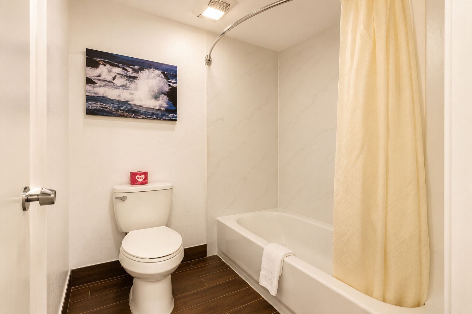 A bathroom with a toilet, a shower, and a painting of waves on the wall.