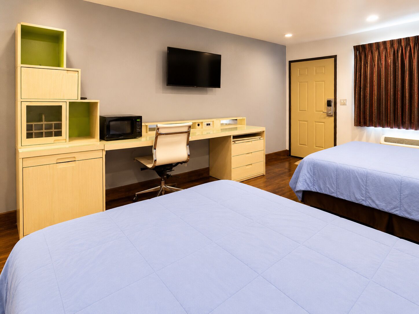 A hotel room with two beds, a desk with a chair, a television, and a door.