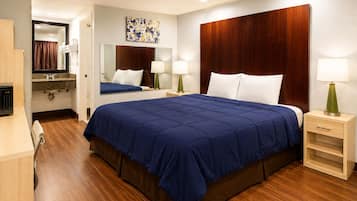 A hotel room with a large bed, wooden headboard, bedside tables with lamps, a mirror, a bathroom with a shower, and a wooden floor.