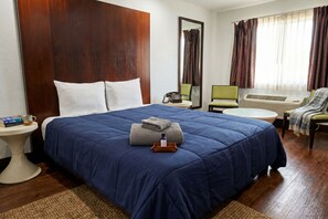 A hotel room with a large bed, a bedside table with a phone, a chair, and a window with curtains. - Century Motel Buena Park Anaheim I-5 (Buena Park)