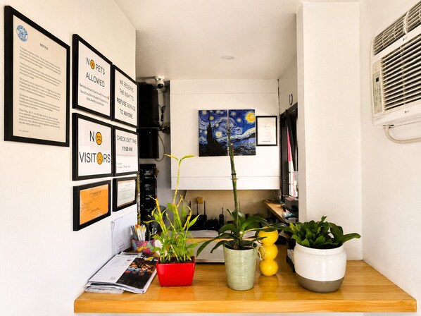 A reception desk with framed notices, a painting, and potted plants. - Century Motel Buena Park Disneyland (Buena Park)