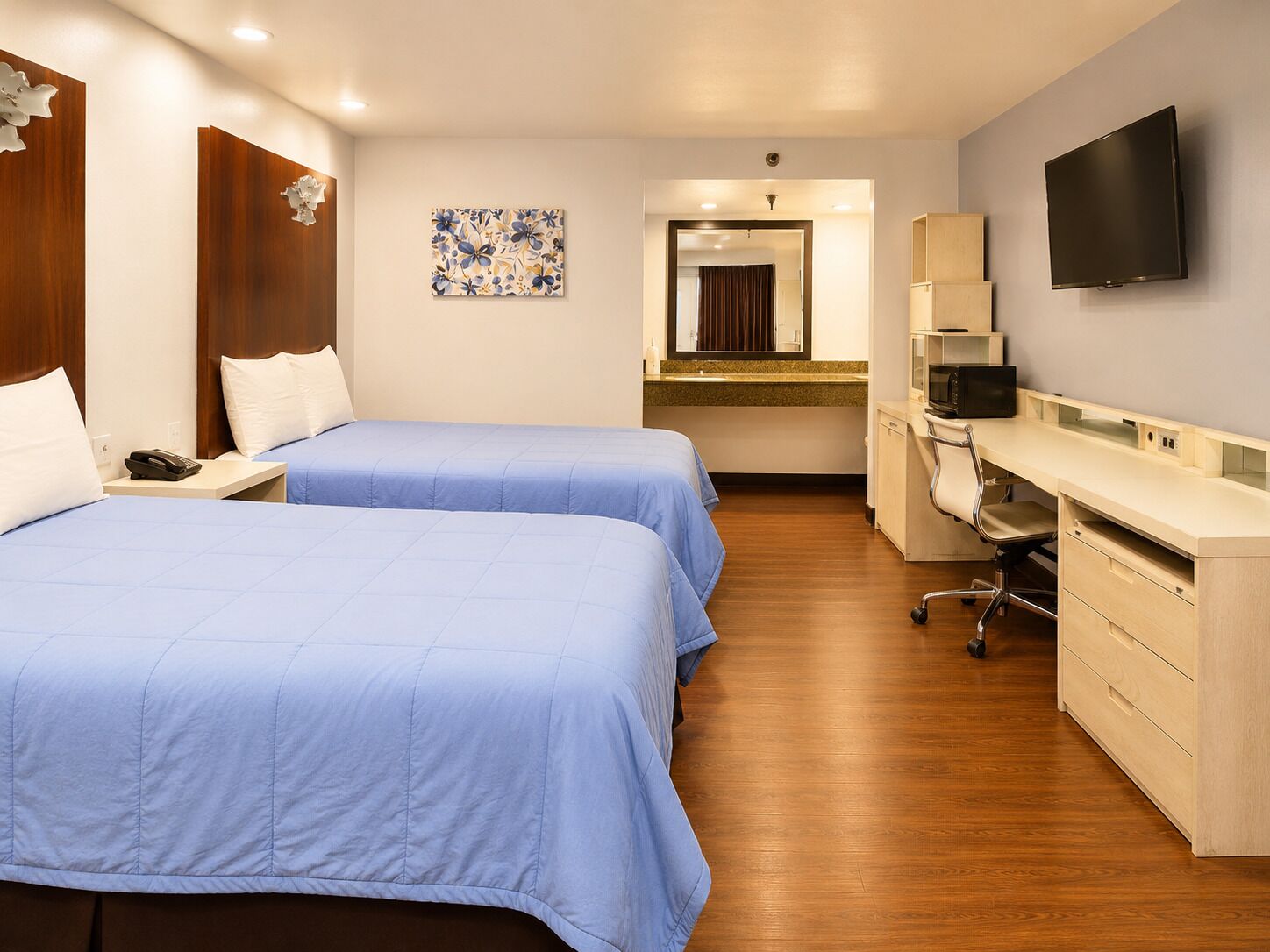 Habitación de hotel con dos camas, un escritorio, televisor y baño visible a través de una puerta abierta.
