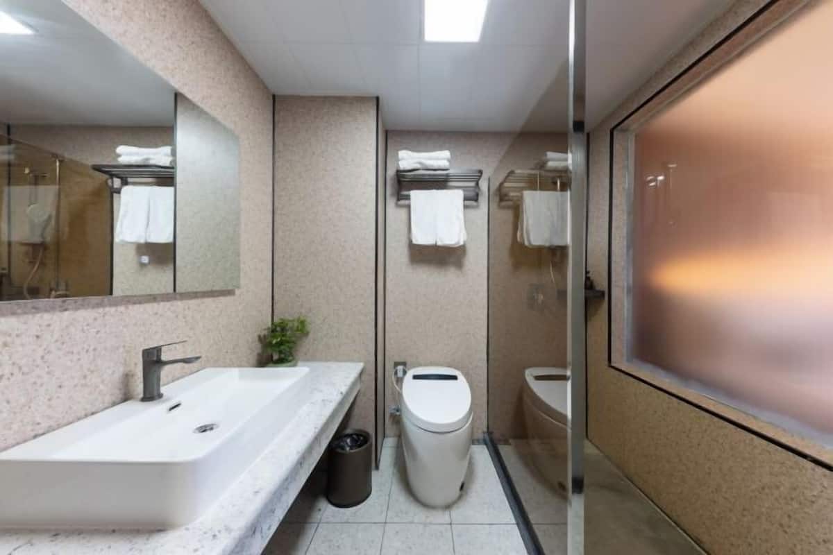 A modern bathroom with a large mirror, a sink, a toilet, and a glass partition.