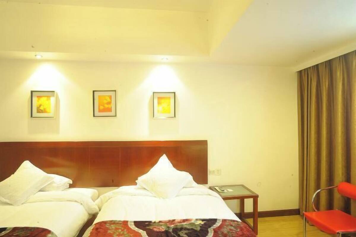 A hotel room with two beds, a wooden headboard, a small table, a red chair, and three framed pictures on the wall.
