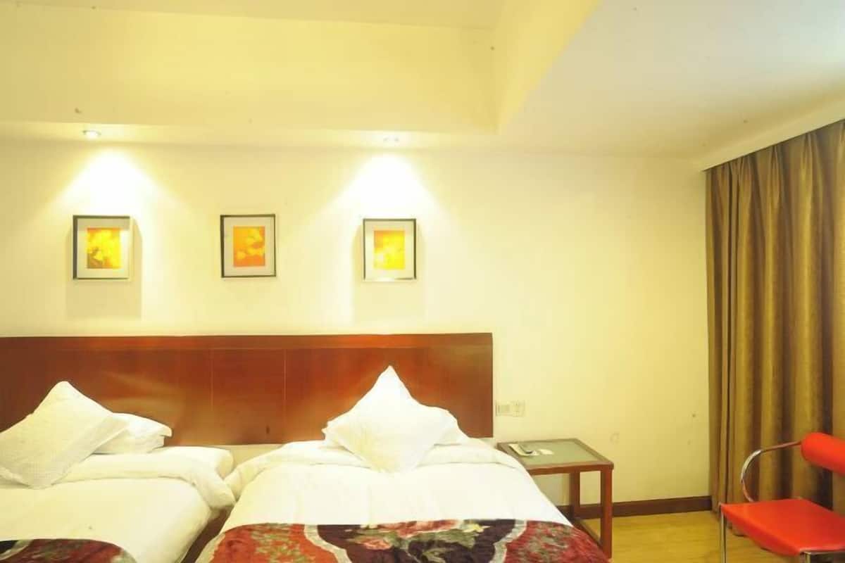 A hotel room with two beds, a wooden headboard, a small table, a red chair, and three framed pictures on the wall.
