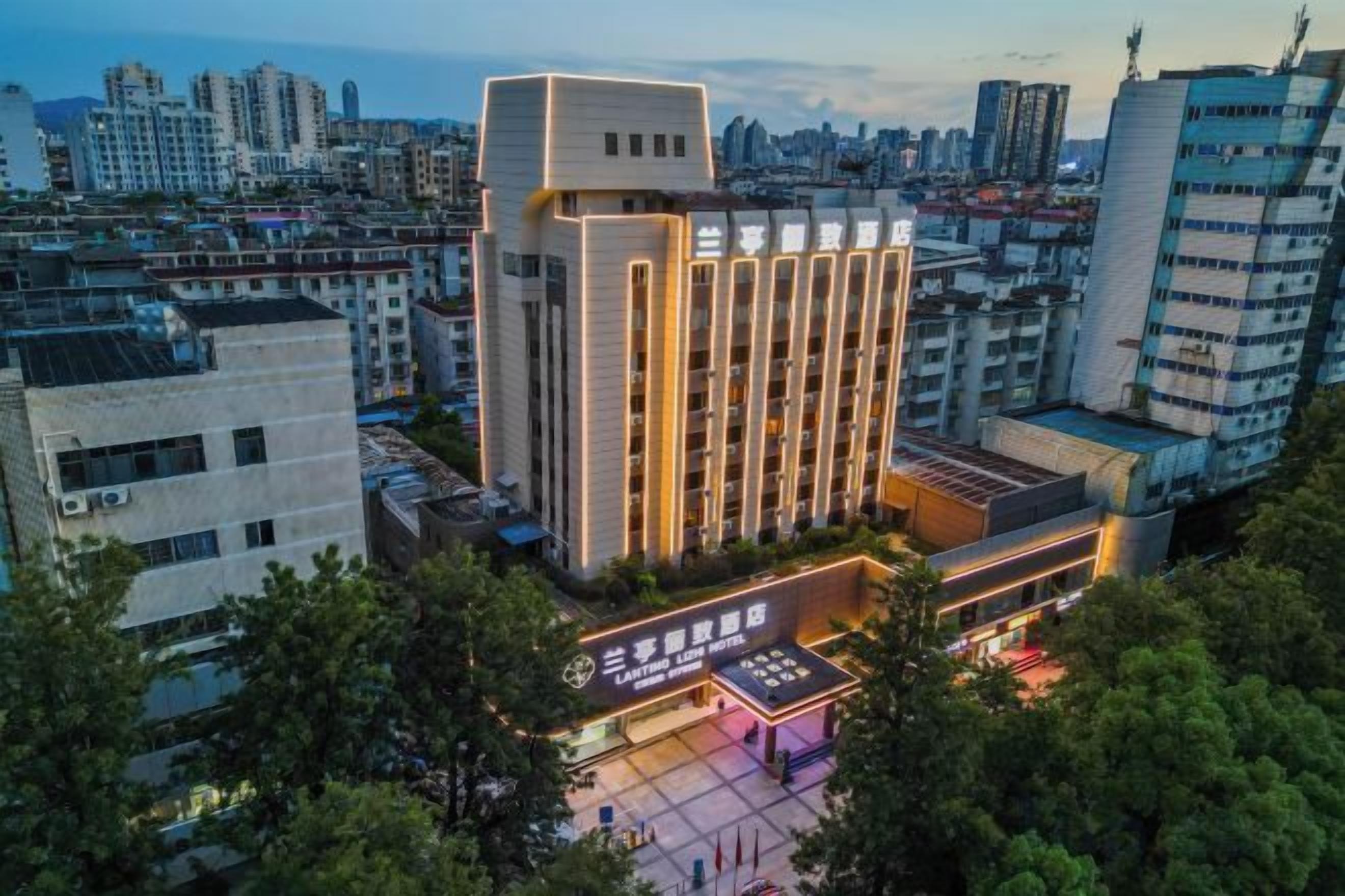 A modern hotel with a prominent central building, surrounded by other structures, and a well-lit entrance area.