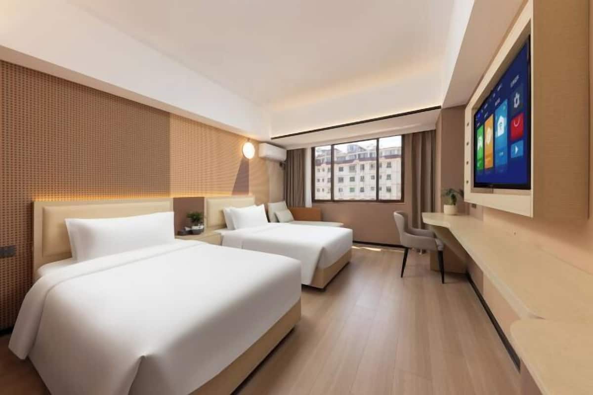 A hotel room with two beds, a desk, a chair, a TV, and a large window.