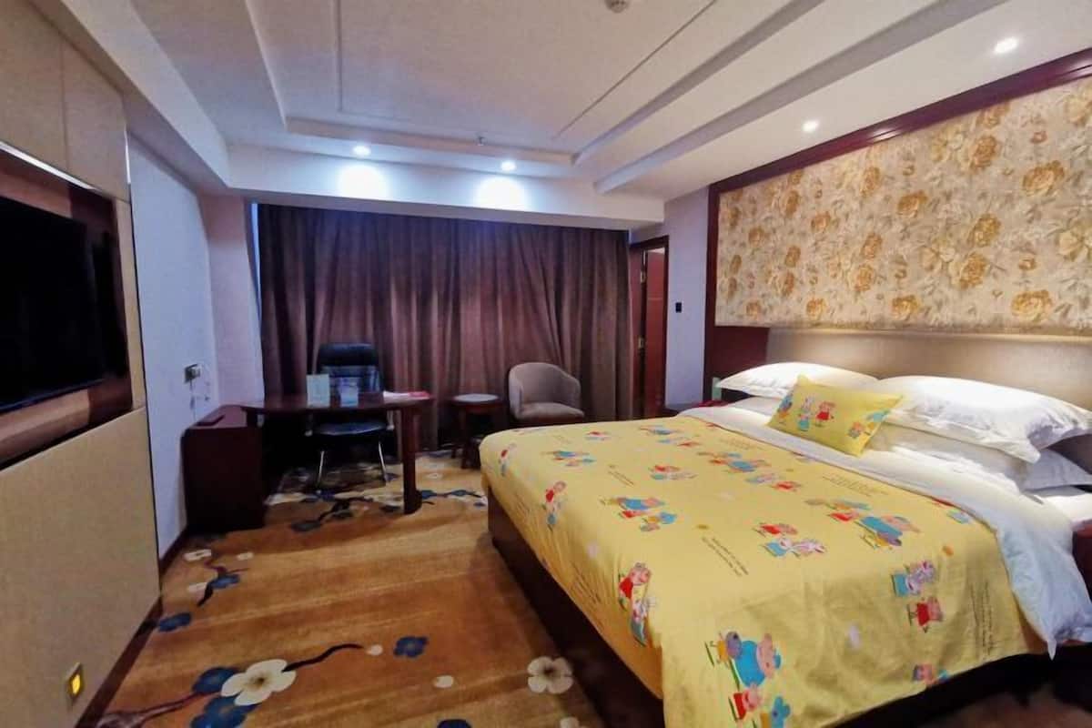 A hotel room with a large bed, a desk, a chair, and a television.