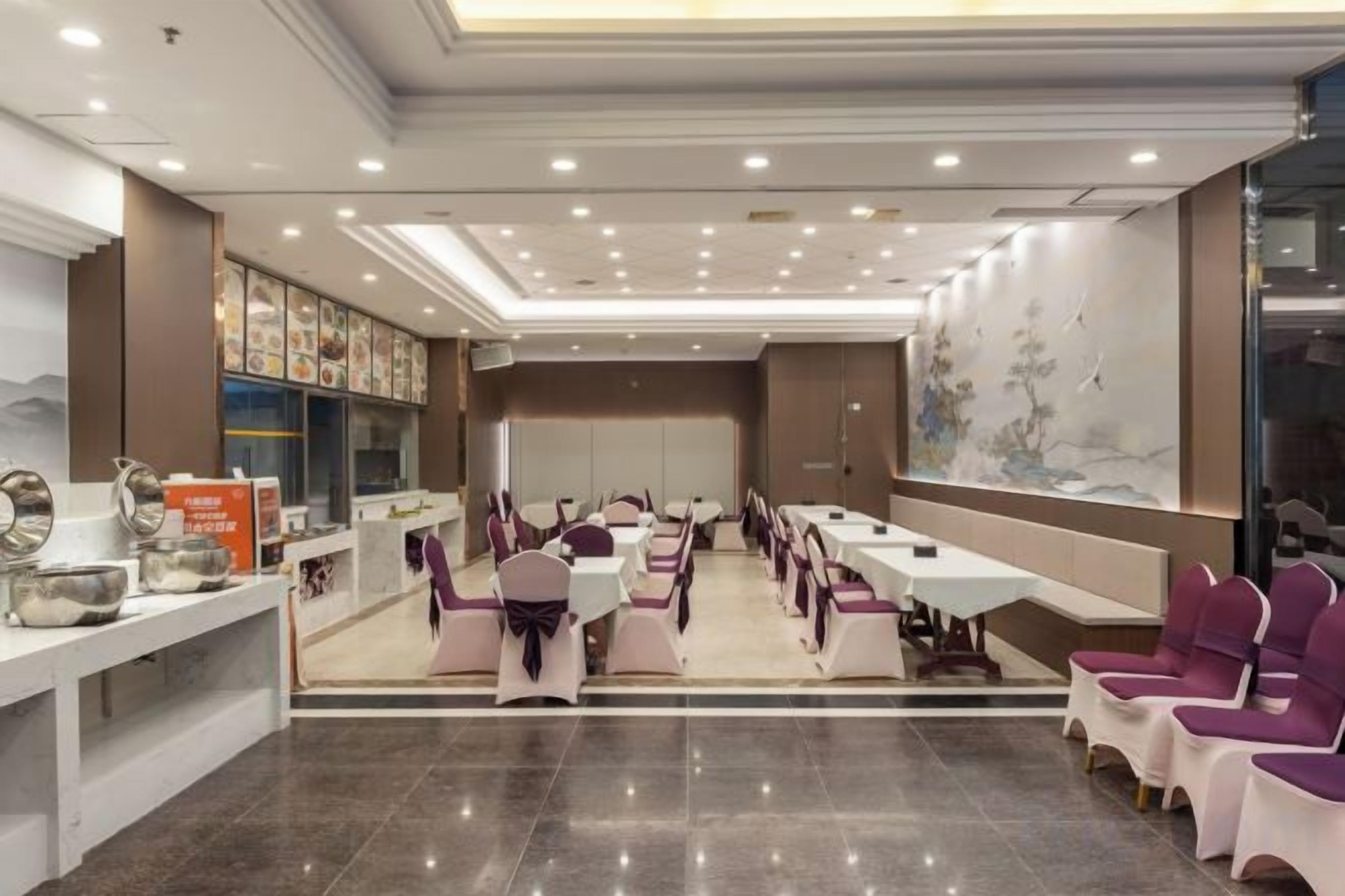 A hotel dining area with multiple tables and chairs, a reception desk, and a wall with artwork.