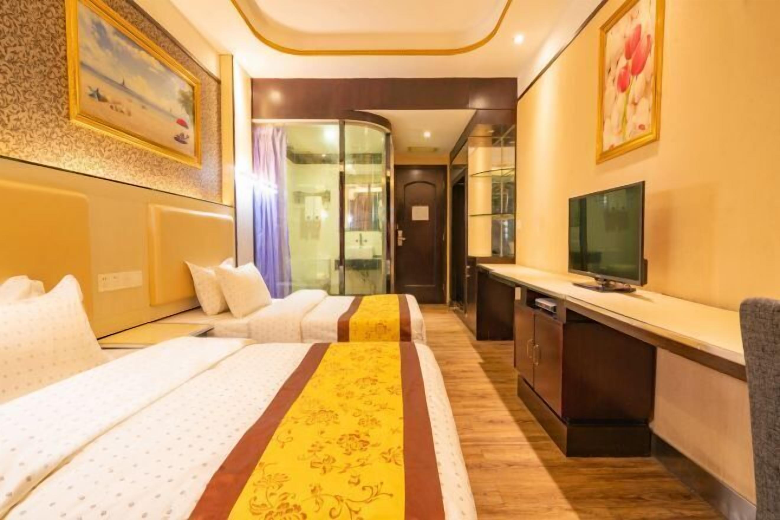 A hotel room with two beds, a TV, a desk, and a glass partition.