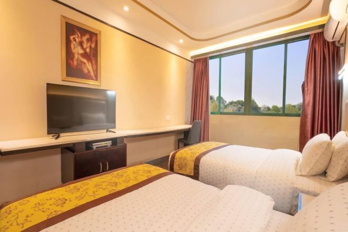 Habitación de hotel con dos camas, televisión, escritorio y ventana con cortinas.