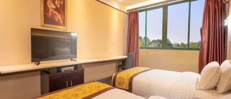 Une chambre d’hôtel avec deux lits, une télévision, un bureau et une fenêtre avec des rideaux.