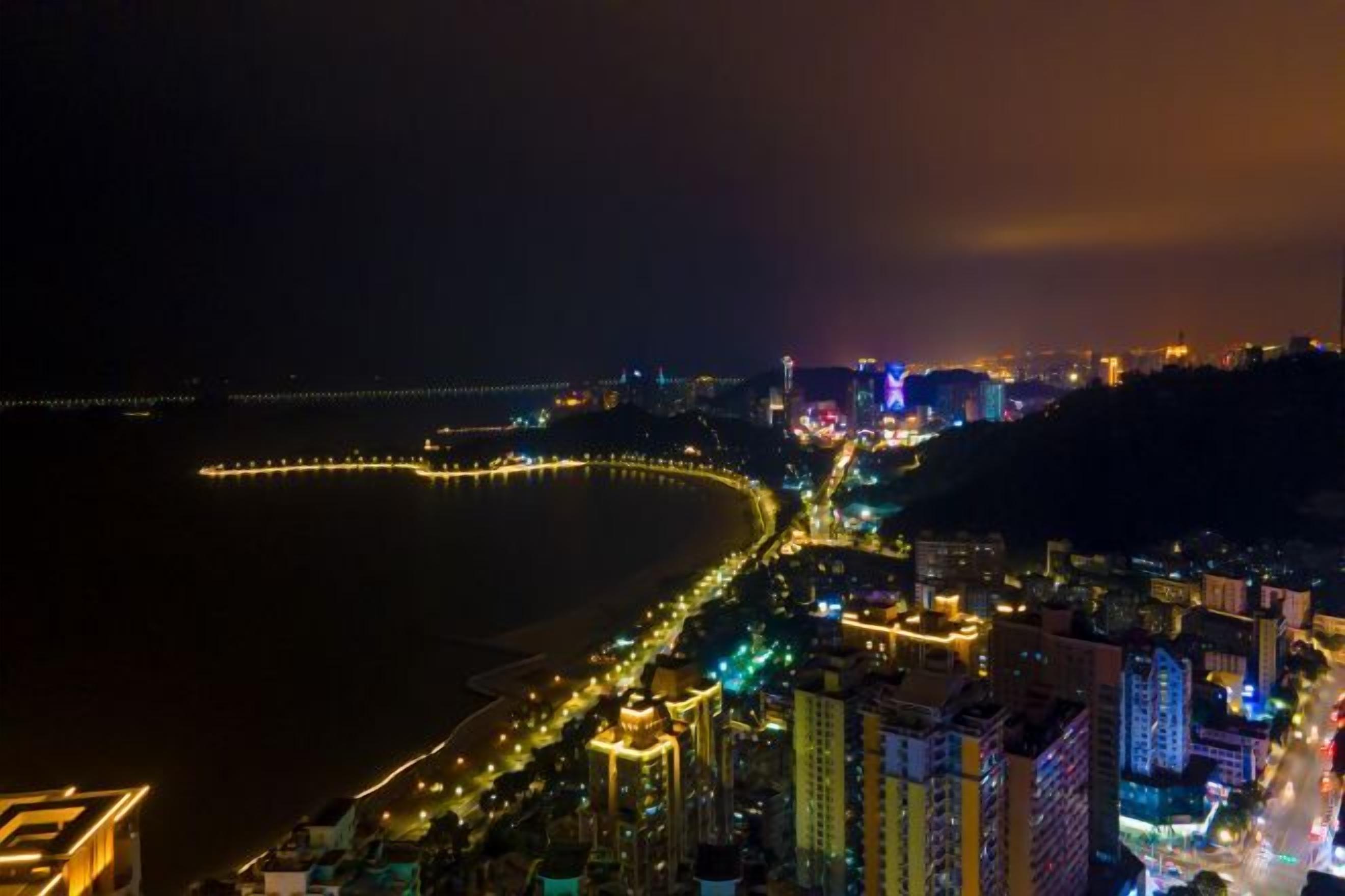 A coastal cityscape at night with illuminated streets and buildings.