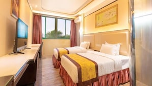 Habitación de hotel con dos camas, un escritorio, un televisor y una ventana con cortinas.