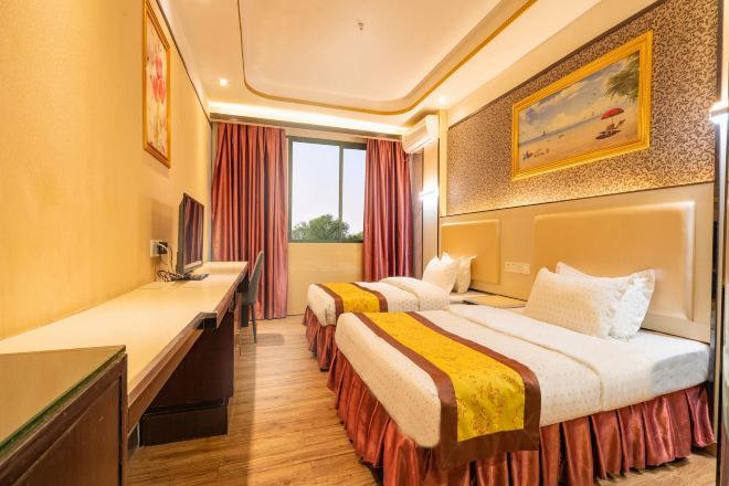 Habitación de hotel con dos camas, un escritorio, una ventana con cortinas y un cuadro en la pared.
