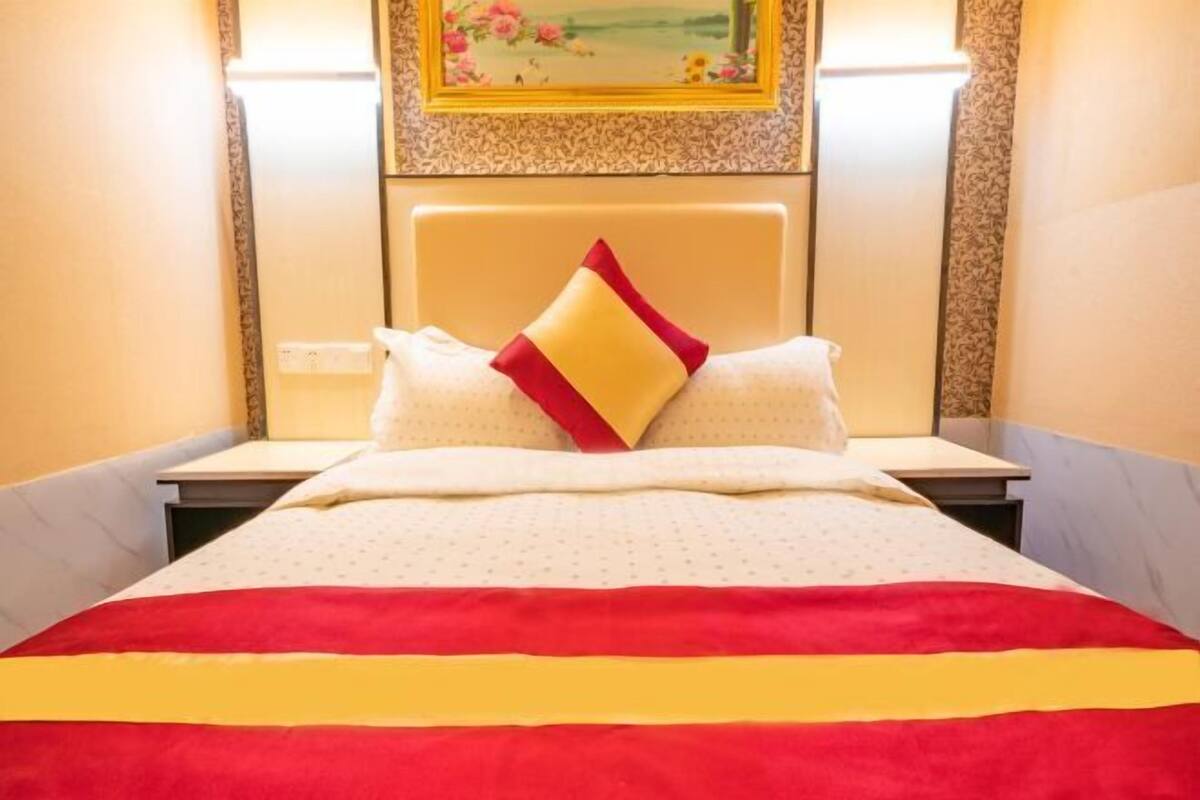 Una cama con colcha a rayas rojas y amarillas, dos almohadas y un cabecero.