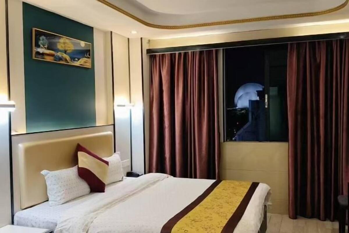 Una habitación de hotel con una cama, una mesita de noche, un cuadro en la pared y cortinas en las ventanas.