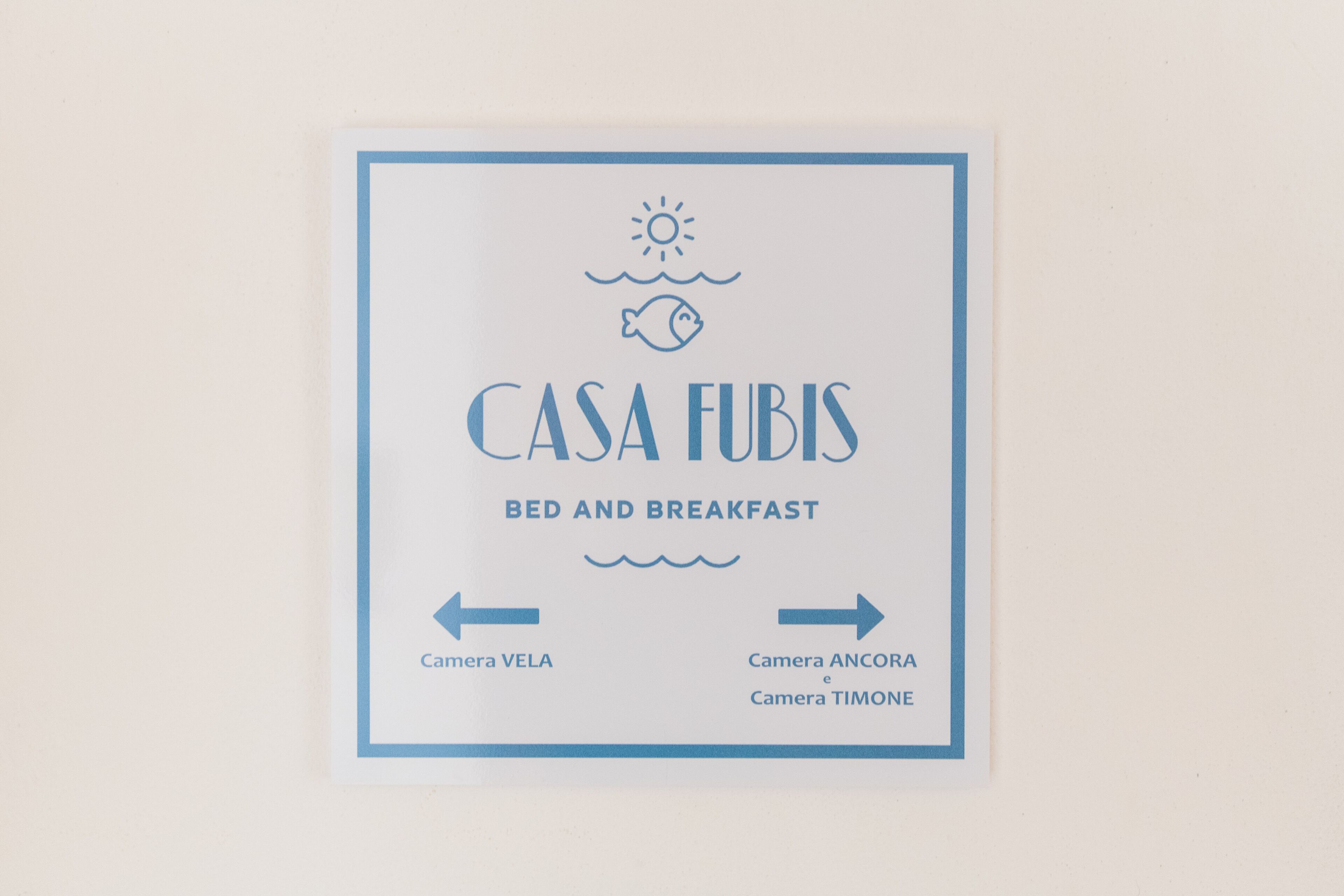 A sign for 'Casa Fubis Bed and Breakfast' with directional arrows to different cameras: VELA, ANCORA, and TIMONE.