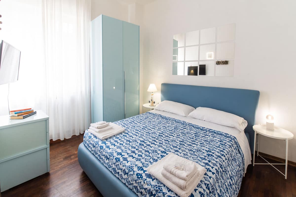 A neatly arranged bedroom with a bed, a nightstand, a wardrobe, and a mirror on the wall.