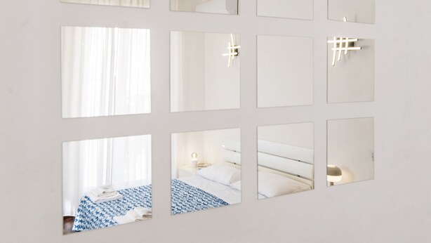 A wall with multiple square mirrors reflecting various parts of a room. - Casa Fubis (Viareggio)