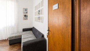 A room with a wooden door, a gray sofa, and a white wall with framed pictures. - Casa Fubis (Viareggio)