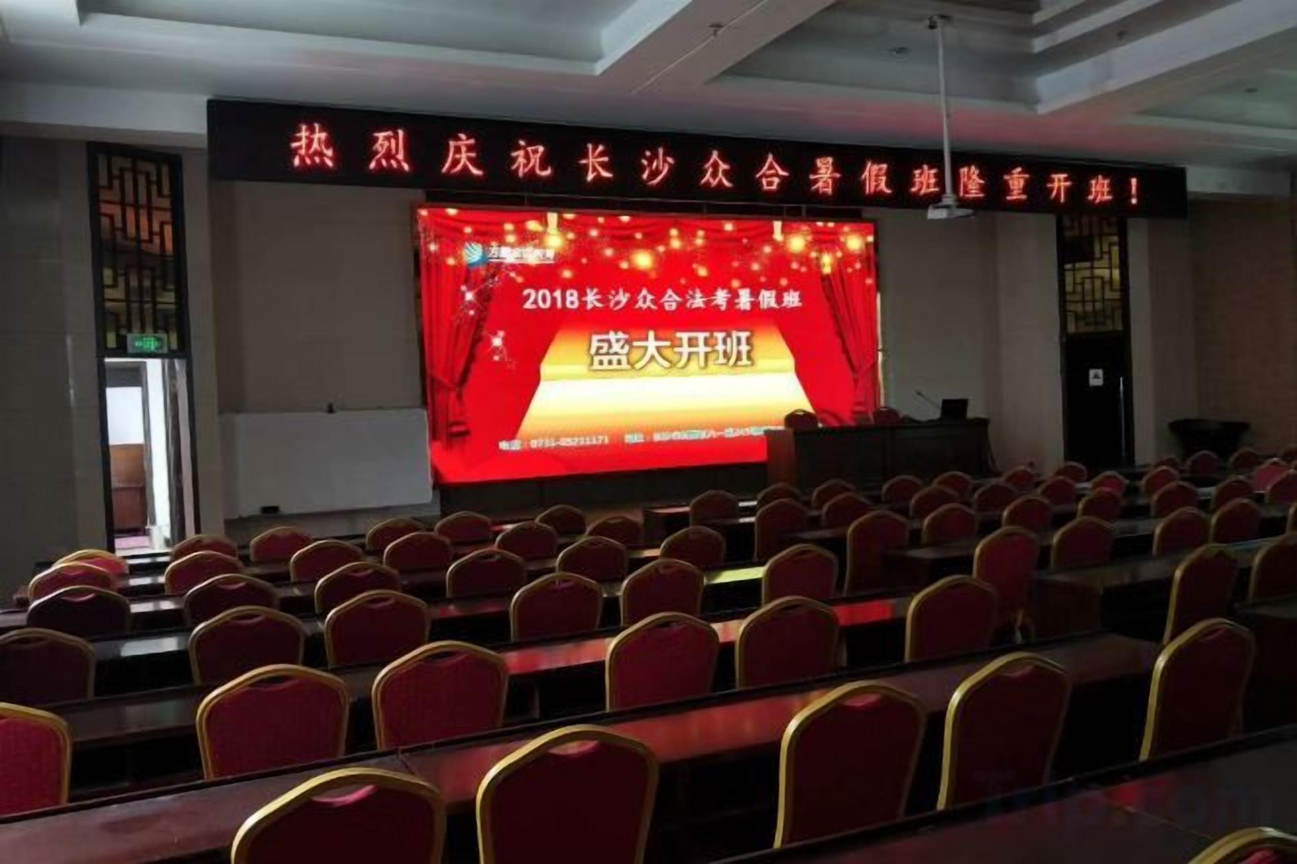 Un salón de conferencias con filas de sillas orientadas hacia un escenario con una pantalla grande que muestra texto.