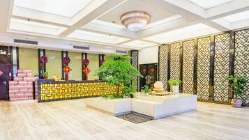 A hotel reception area with a reception desk, a large potted plant, and a decorative wall with vertical panels.