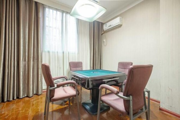 Una habitación con mesa de billar, cuatro sillas, una lámpara en el techo y un ventanal con cortinas.