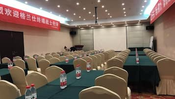 Un salón de conferencias con filas de sillas, mesas y botellas de agua.