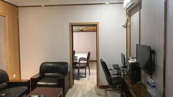 Una habitación de hotel con sofá, escritorio, computadora, televisión y una mesita.