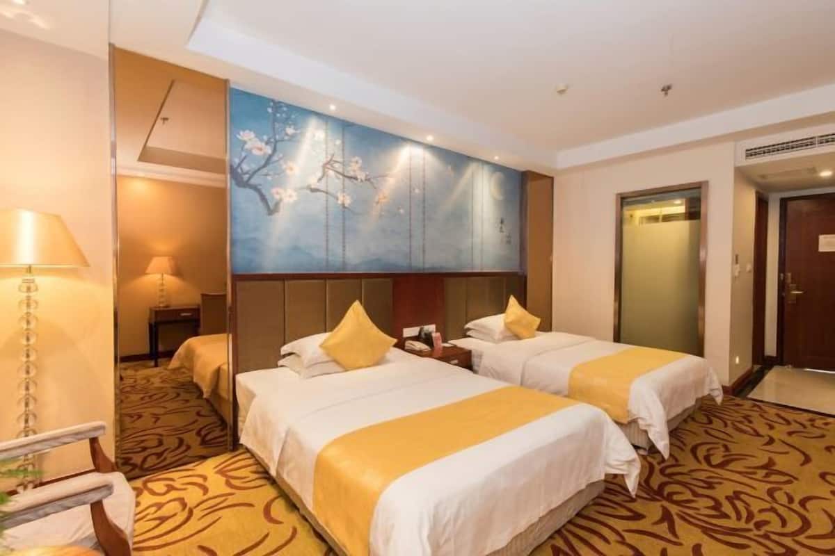 A hotel room with two beds, a large wall painting, a carpeted floor, and a door to the bathroom.